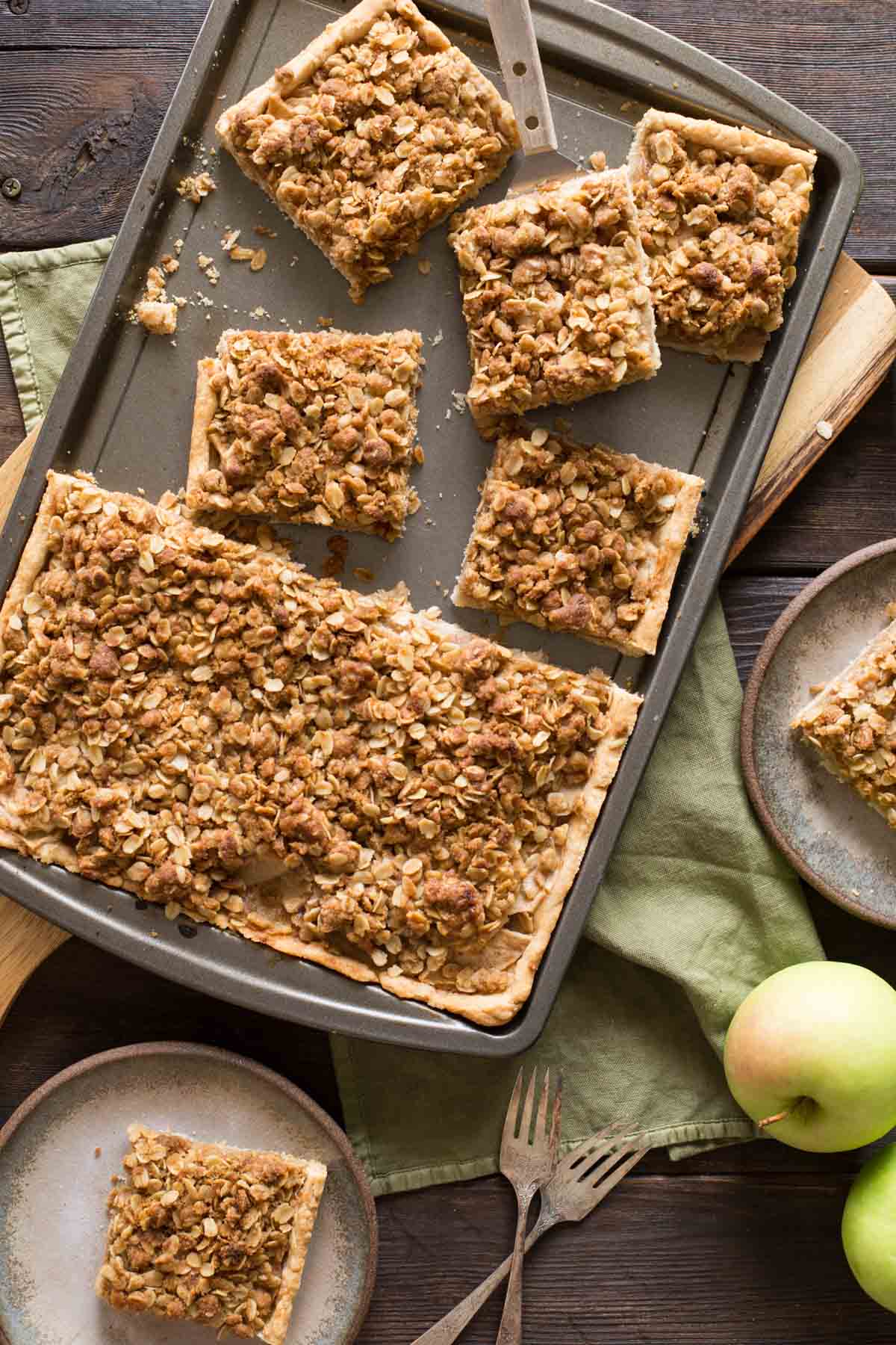 A top down view of a Dutch Apple Slab Pie with a few pieces cut out and fresh apples scattered around. 