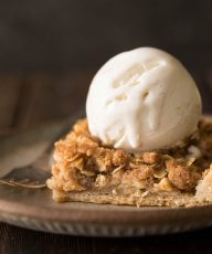 A close up view a piece of Dutch Apple Slab Pie with a scoop of vanilla ice cream on top.