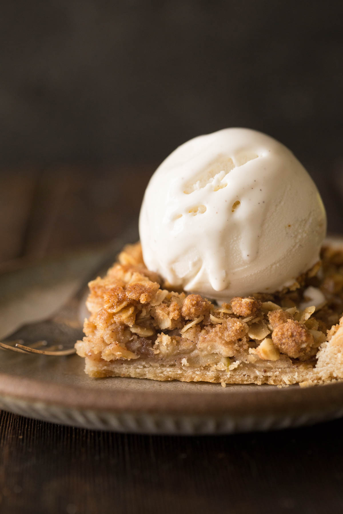 A close up view of a square of Dutch Apple Slab pie on a plate with a scoop of vanilla ice cream on top. 