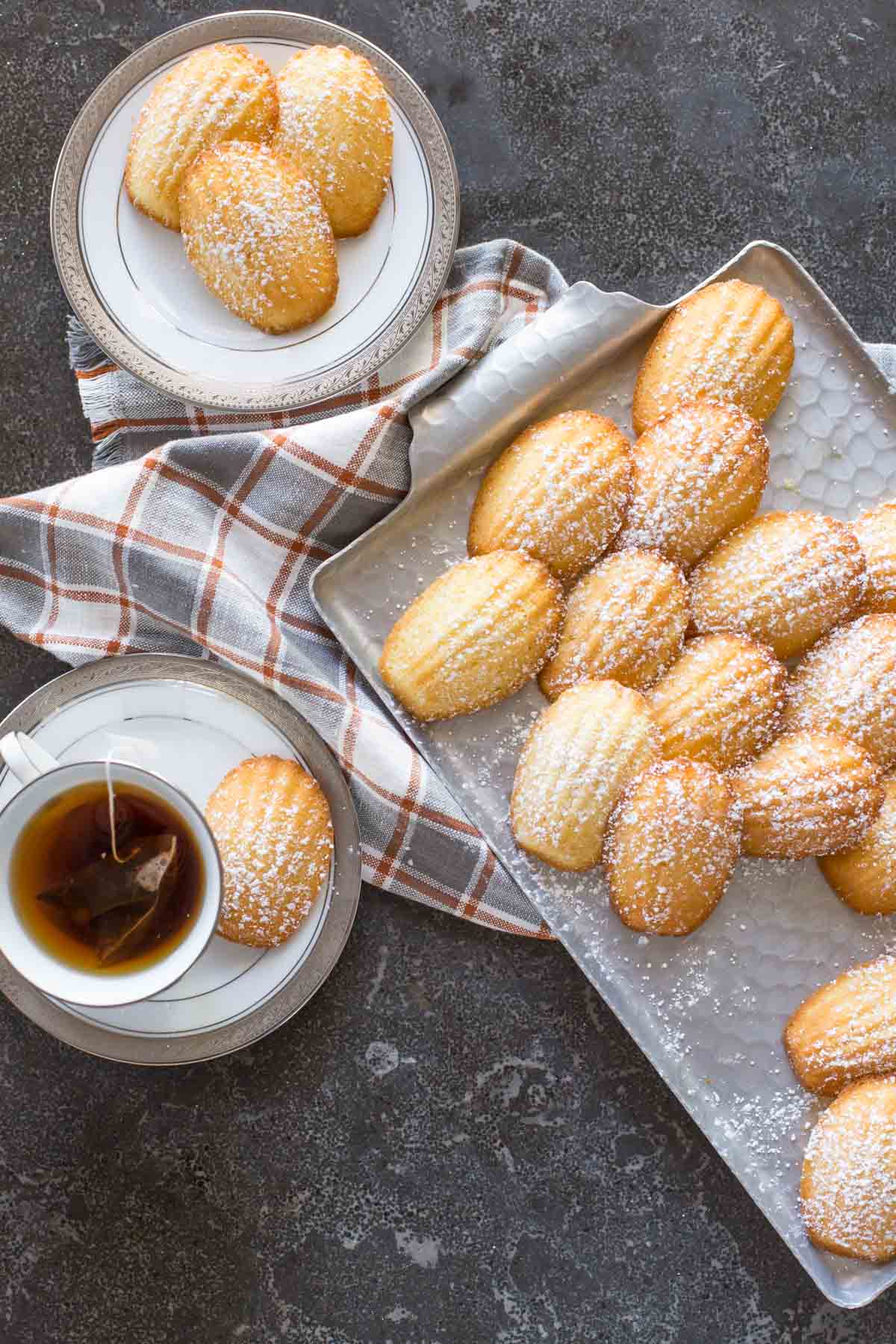 Overhead view of a platter of Lemon Vanilla Madeleines with a cup of tea. 