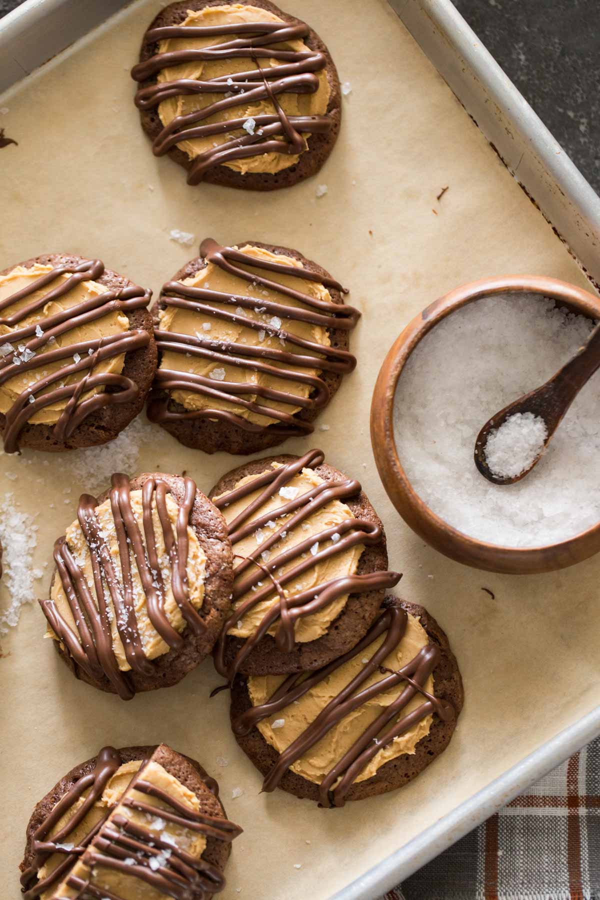 Peanut Butter Buckeye Brownie Cookies on a baking sheet with a bowl of flakey sea salt.