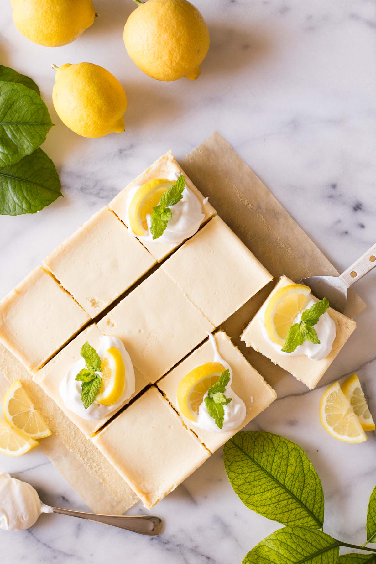 Overhead view of the Best Creamy Lemon Bars on a marble slab topped with lemon slices, fresh mint and whipped cream.