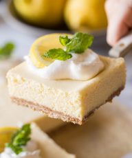 Close up view of the Best Creamy Lemon Bars on a marble slab topped with lemon slices, fresh mint and whipped cream.