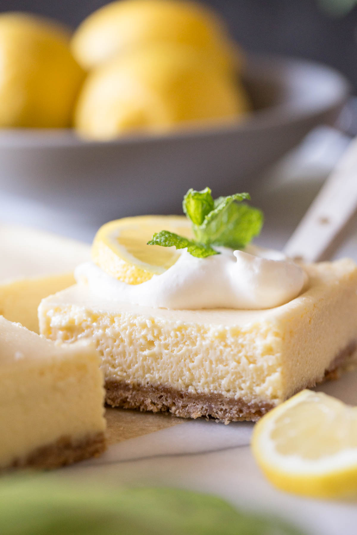 Close up view of the Best Creamy Lemon Bars on a marble slab topped with lemon slices, fresh mint and whipped cream.