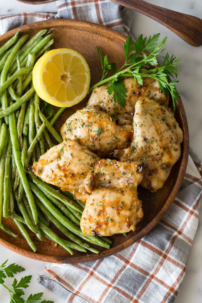 Overhead shot of Best Ever Chicken Marinade on a wooden platter with green beans and lemon. 
