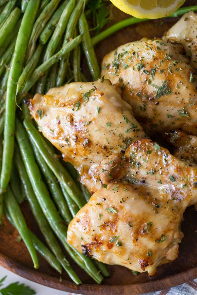 Overhead shot of Best Ever Chicken Marinade on a wooden platter with green beans and lemon. 
