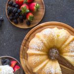 Kentucky Butter Cake on wooden cake stand with whipped cream and berries on a grey background.