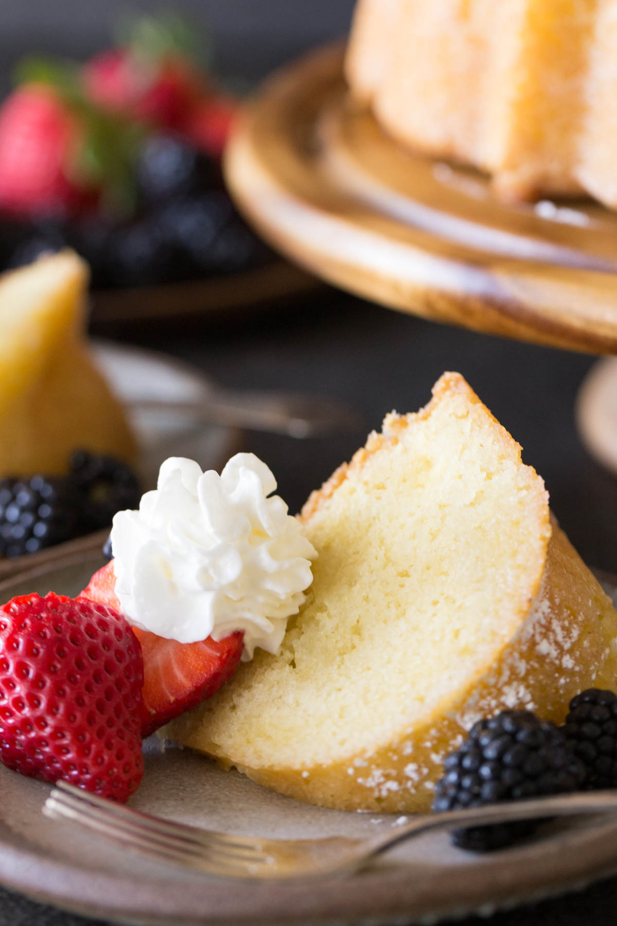 Kentucky Butter Cake on wooden cake stand with whipped cream and berries on a grey background. 