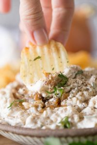 Chip dipping into bowl of Roasted Onion and Caramelized Onion Dip.