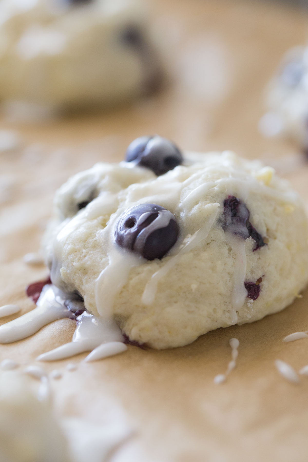 Close up shot of a Glazed Lemon Blueberry Muffin Top on parchment paper. 