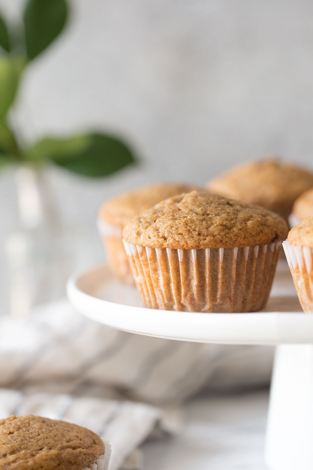 Cinnamon Applesauce Muffins on a white cake stand with a white background. 