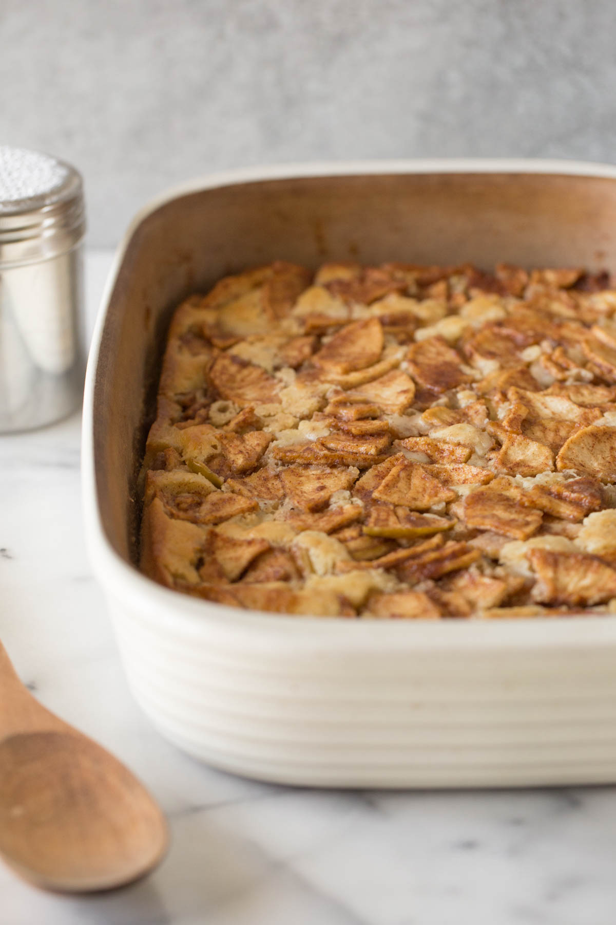 Cream colored baking dish of Apple Cobbler with a grey background. 