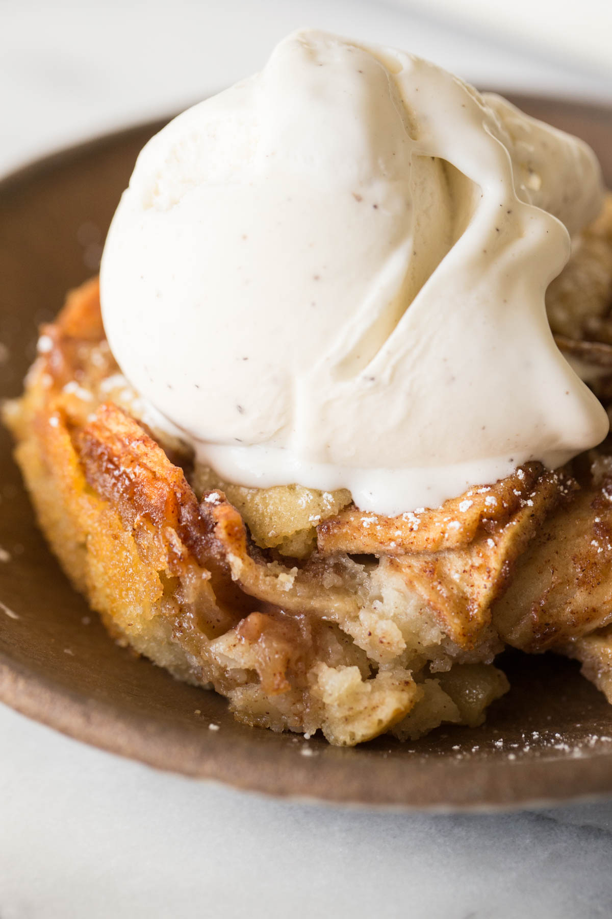 Close up view of bowl full of Apple Cobbler with a scoop of vanilla ice cream on top. 