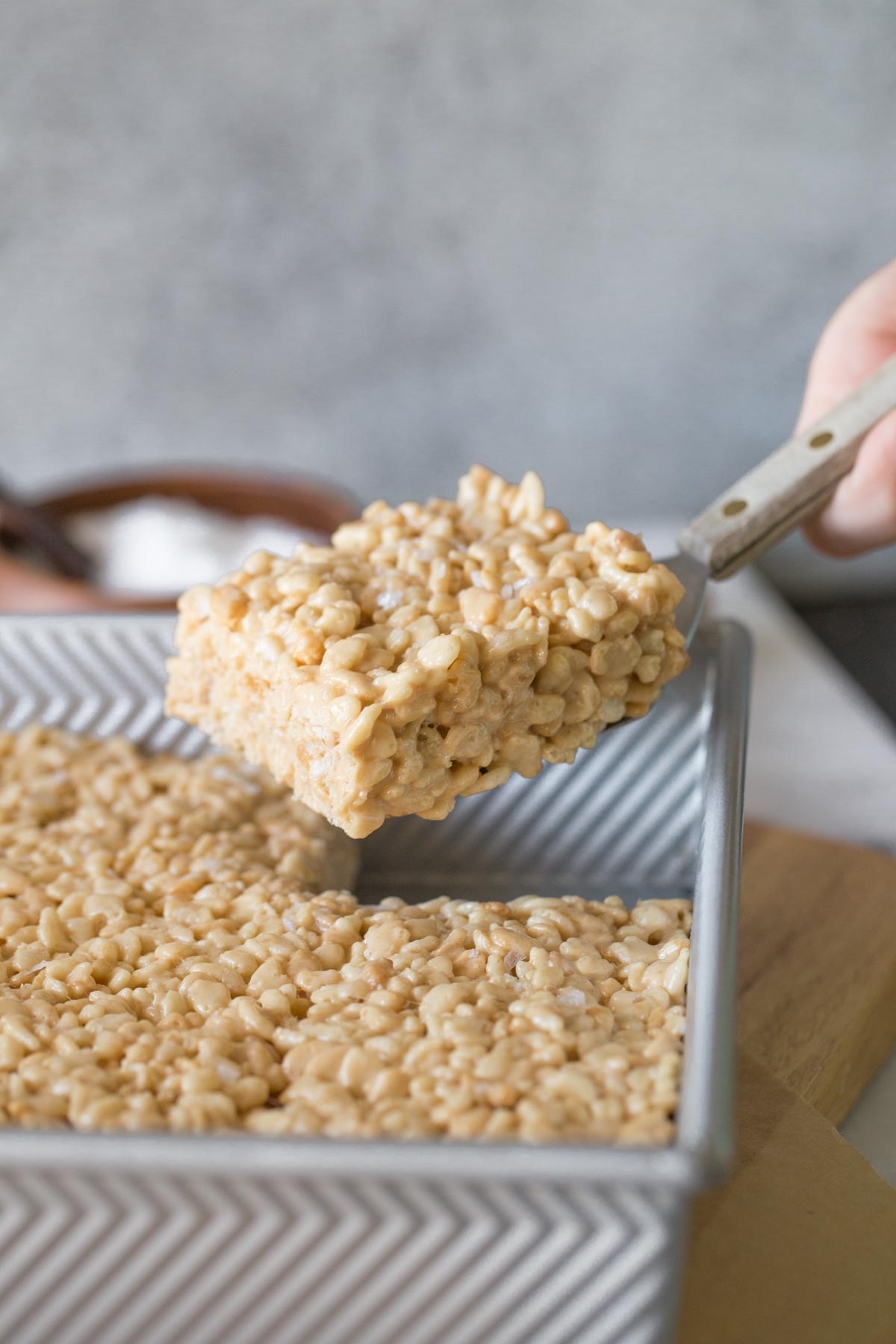 Salted Caramel Rice Krispie Treat being lifted out of a pan with a grey background. 
