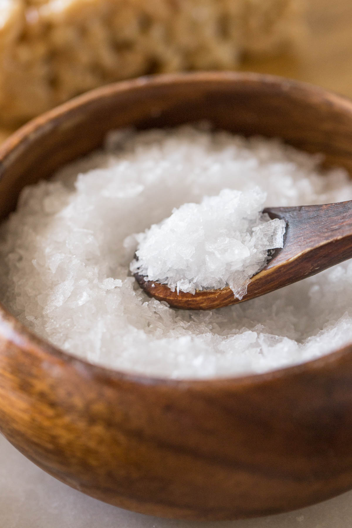 Close up view of bowl of flakey sea salt with wooden spoon. 