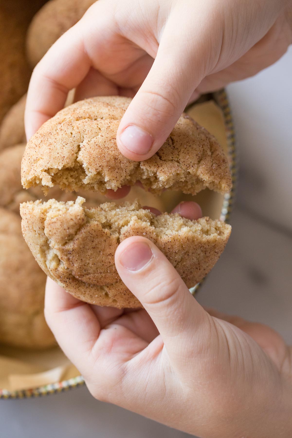 A child's hand breaking open a Super Soft Snickerdoodle. 