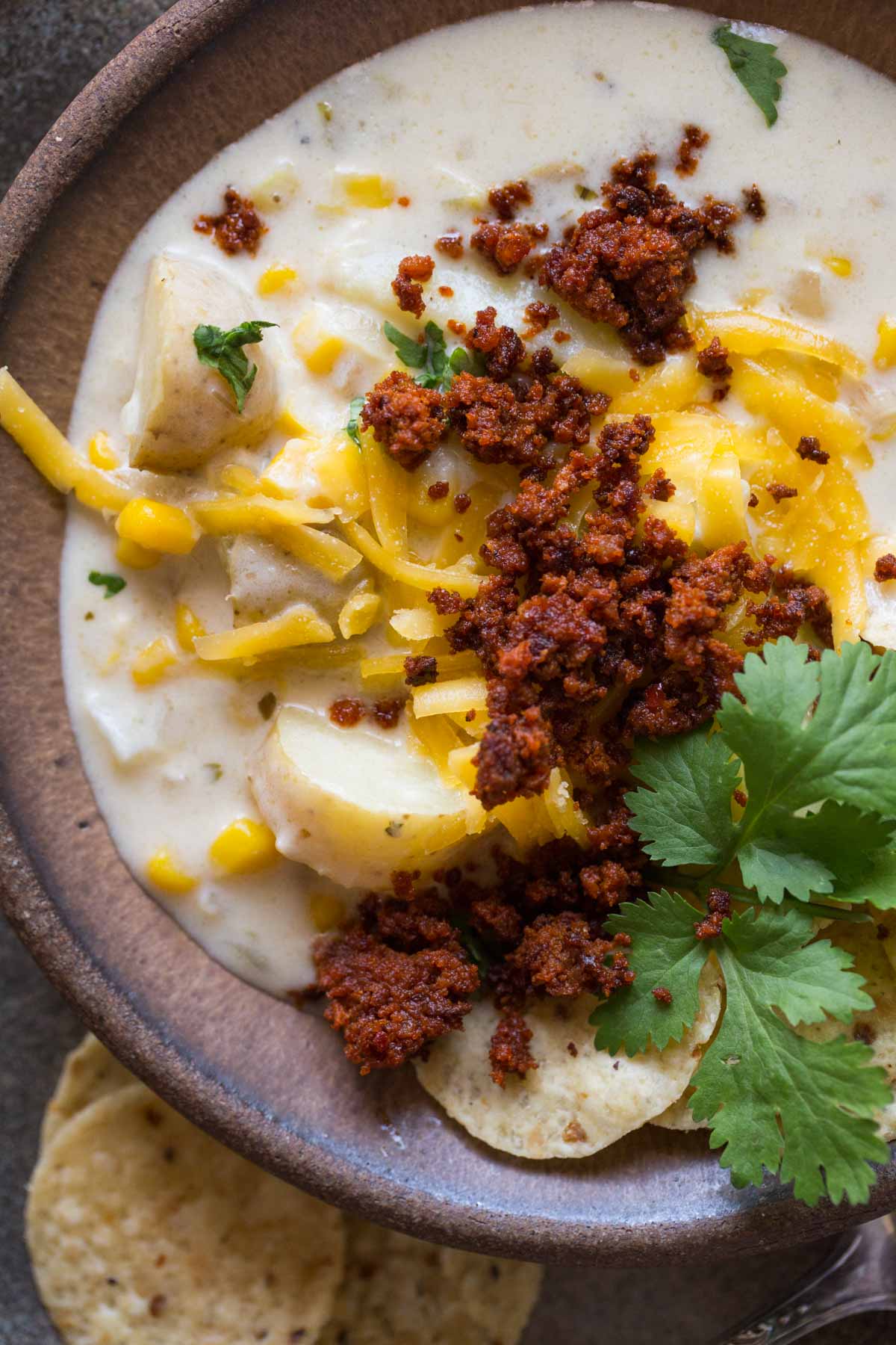 Overhead view of Creamy Corn Chowder With Chorizo in a brown bowl topped with cilantro and cheese. 