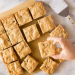 Overhead view of blondies with a child's hand taking one.