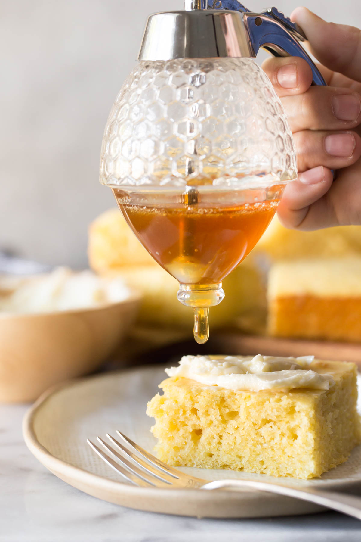 Honey drizzle over a slice of Easy Homemade Cornbread on a plate with fork in foreground. 