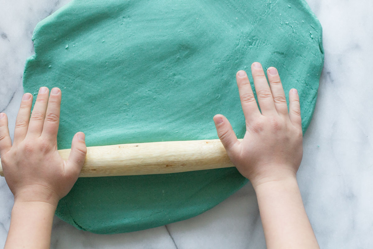 Overhead view of blue playdough being rolled out. 