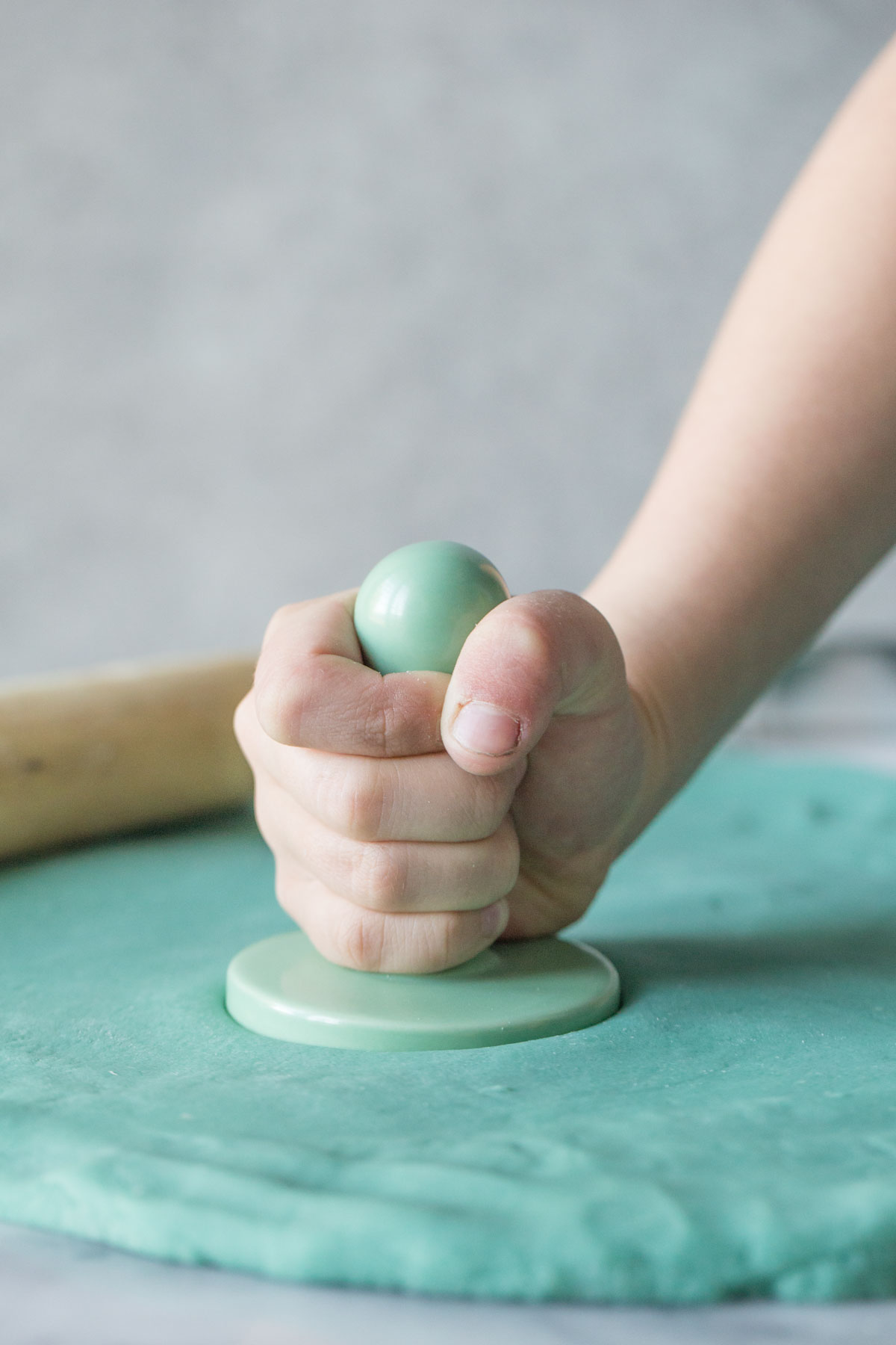 A child's hand using a stamp in blue playdough. 