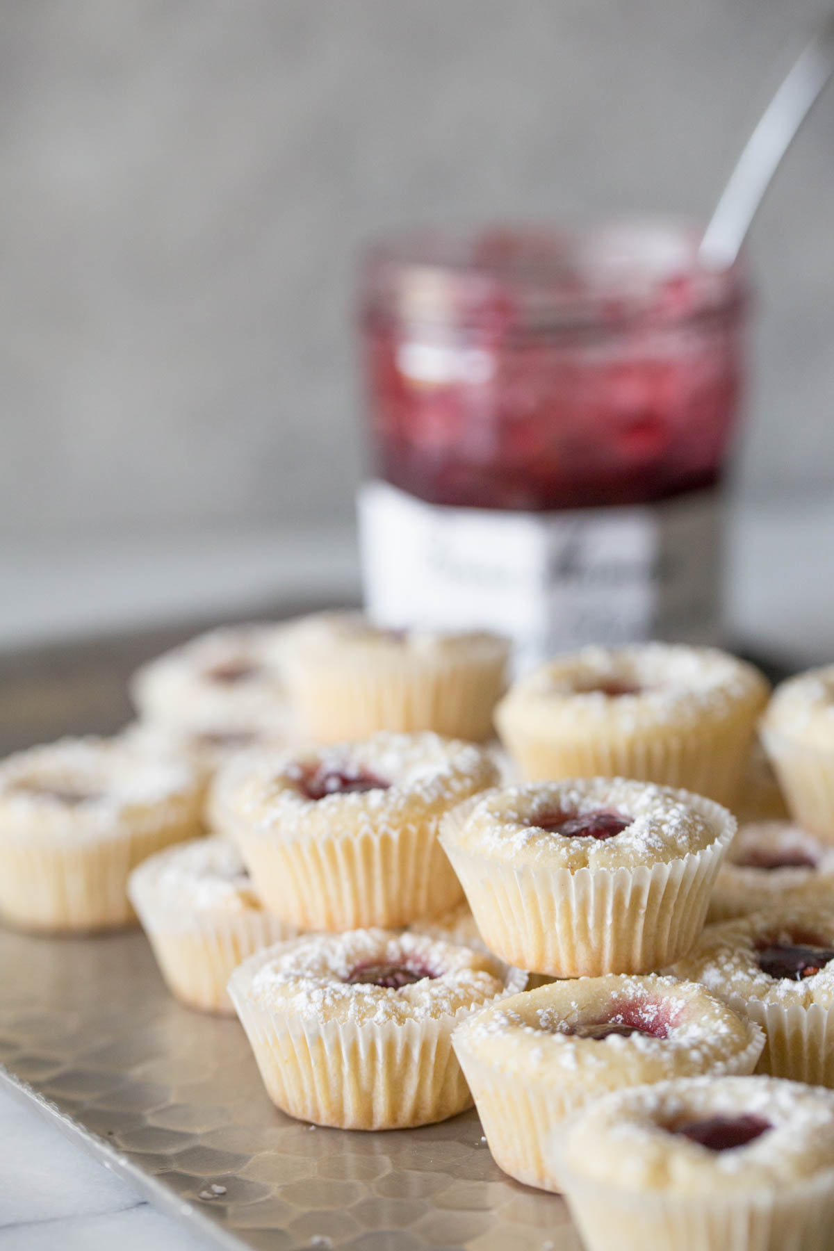 Stacked Mini Raspberry Almond Tarts on a sliver tray with a jelly jar in the background. 