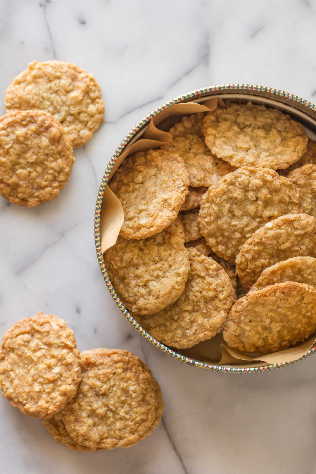 Overhead shot of Buttery Coconut Oatmeal Cookies in a container, with more cookies next to the container on a marble background.  