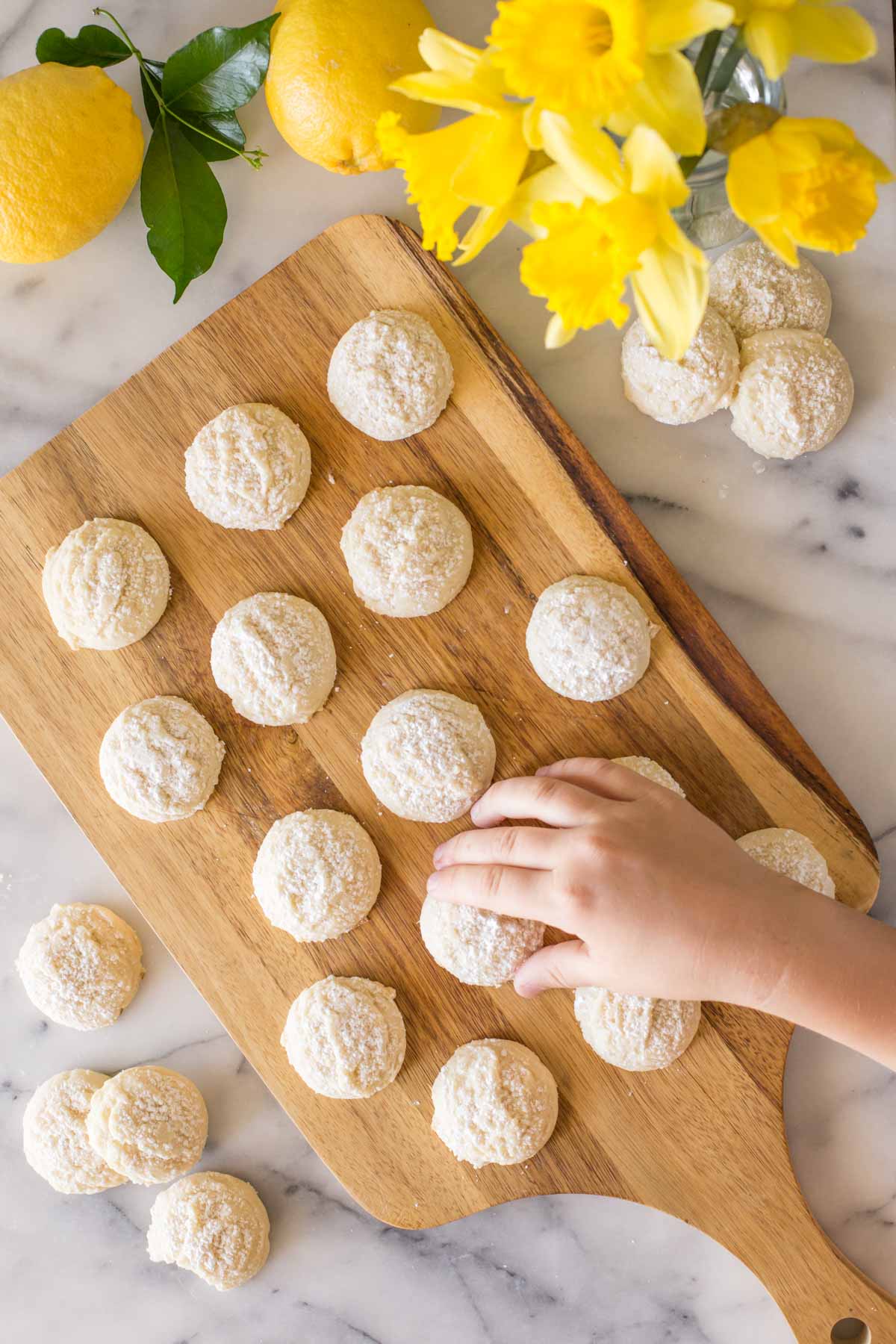Hand reaching for Lemon Cookie on a wooden cutting board. 