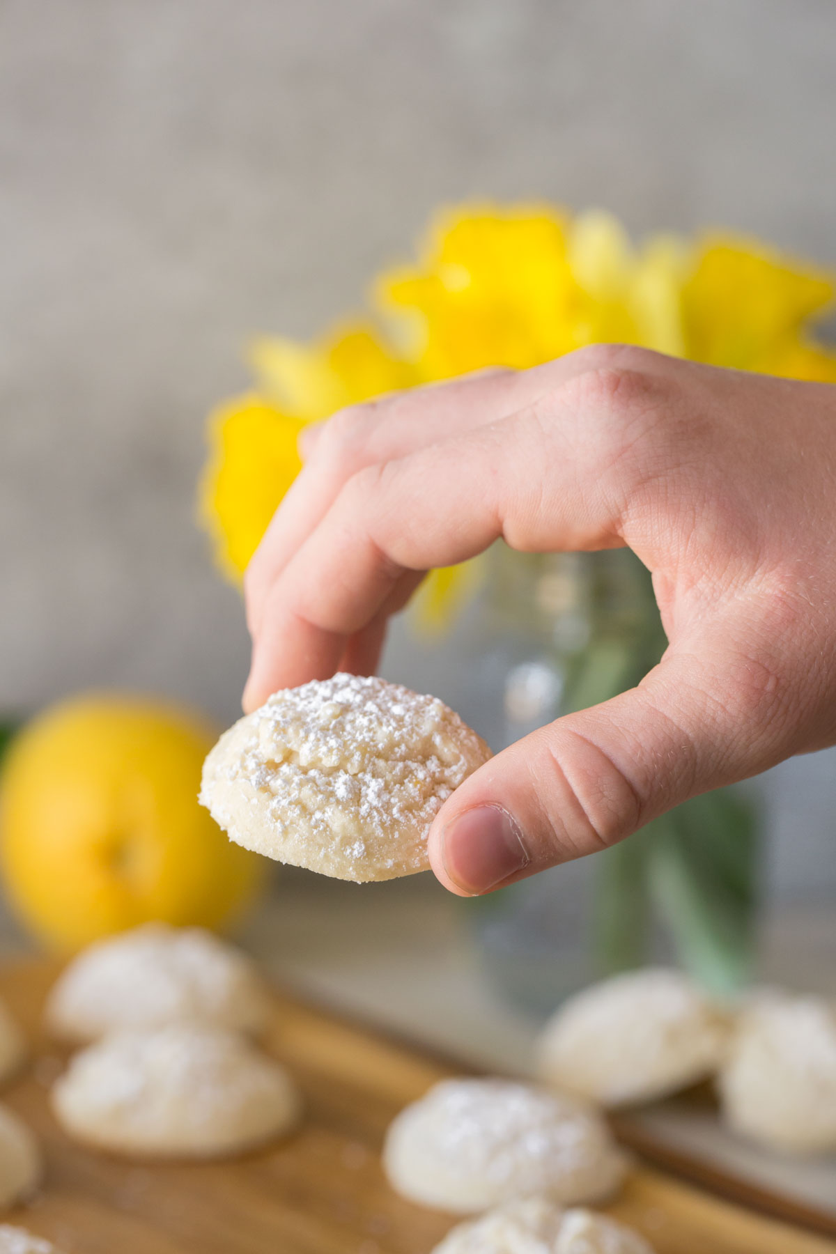 Hand holding Lemon Cookie with yellow daffodils in the background. 