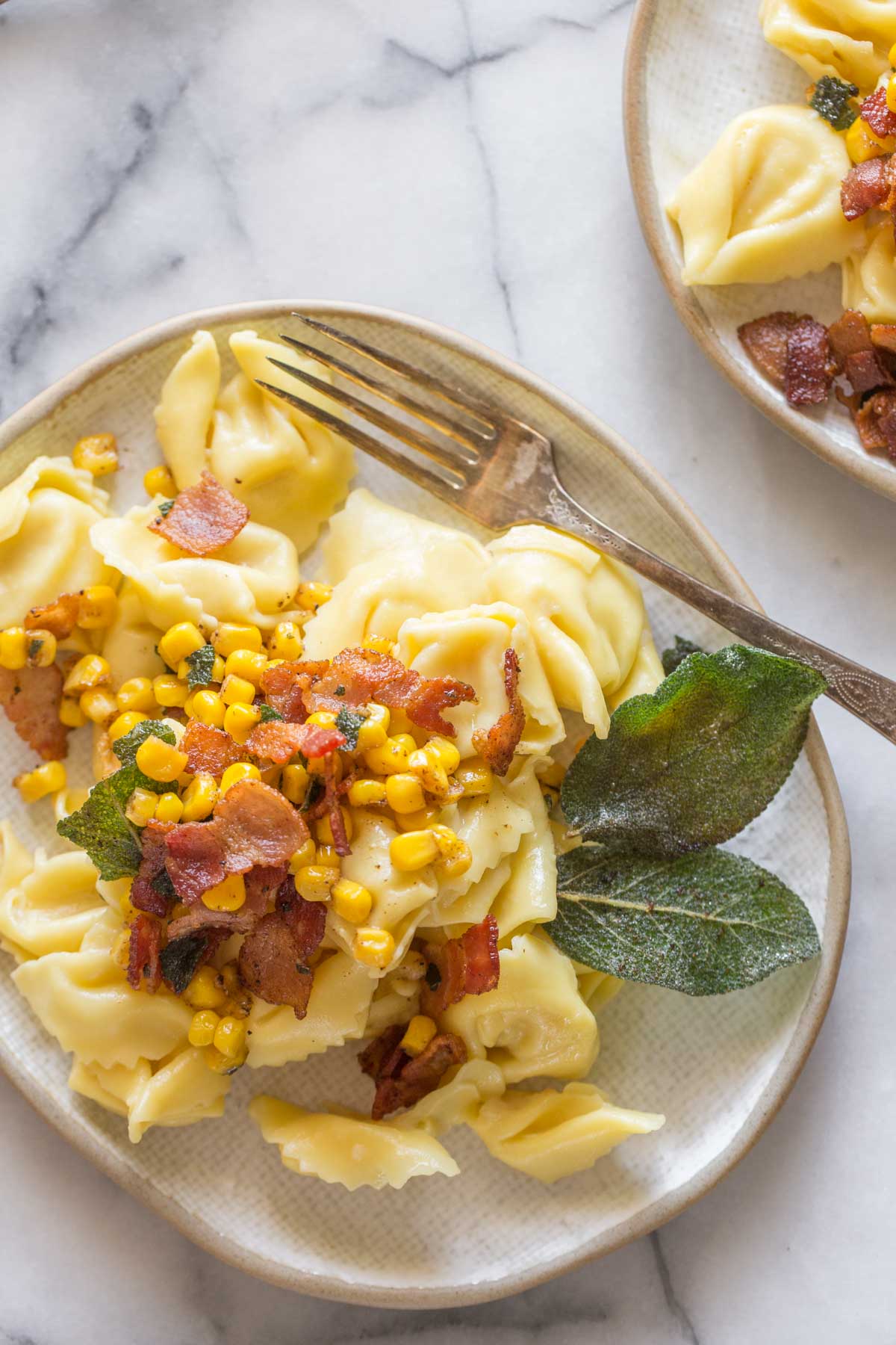 Overhead shot of a plate of Creamy Tortellini With Bacon and Corn on a marble background.  