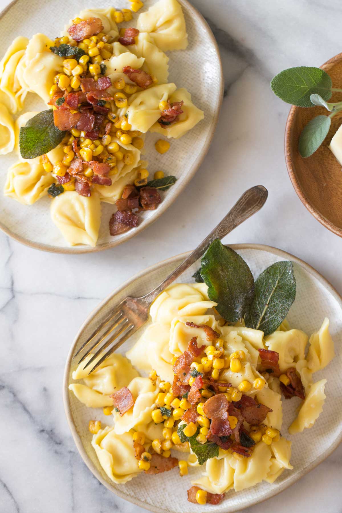 Overhead view of two plates of Creamy Tortellini With Bacon and Corn on a marble background.  