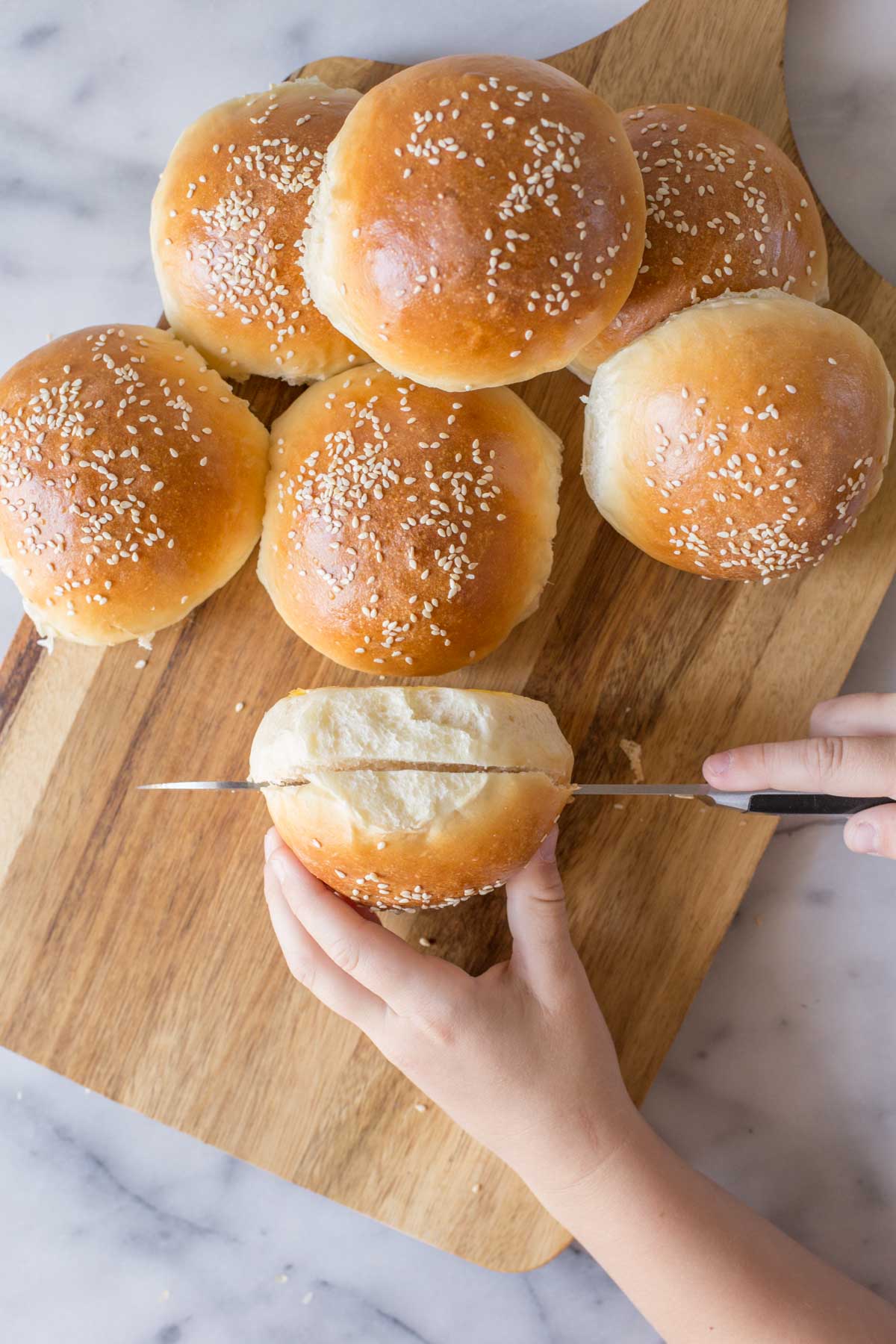A Sourdough Hamburger Bun being cut open on a wooden cutting board with more buns next to it.  