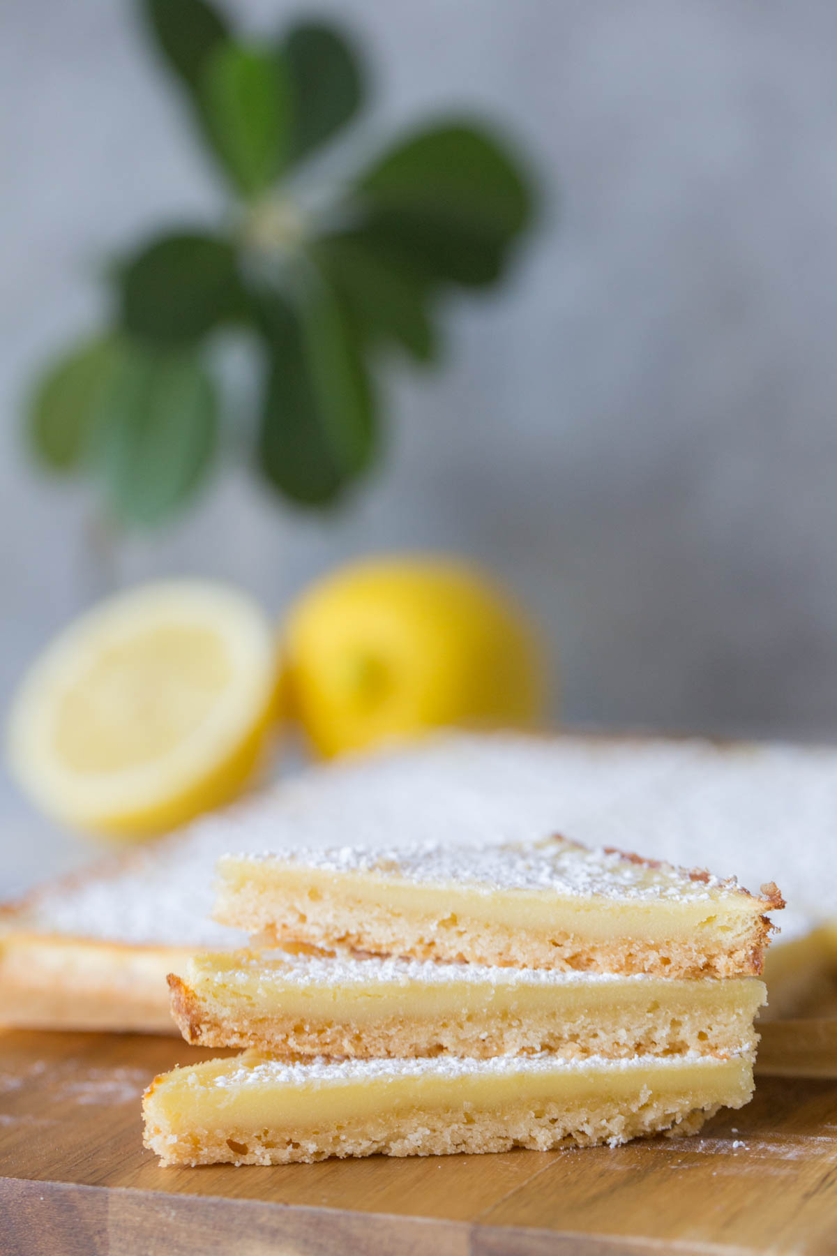 Close up shot of three Swedish Lemon Bars stacked on a wooden cutting board.  