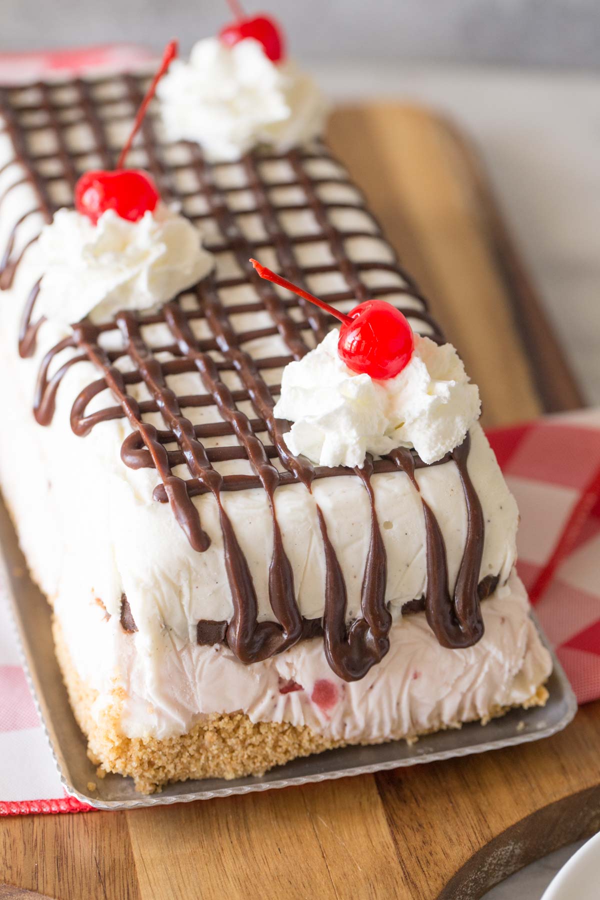 Banana Split Ice Cream Cake on a serving tray sitting on a wooden cutting board. 