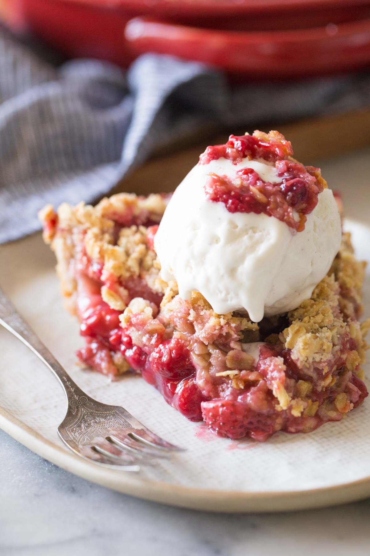 Close up shot of a slice of Berry Crumble Pie topped with a scoop of vanilla ice cream.  