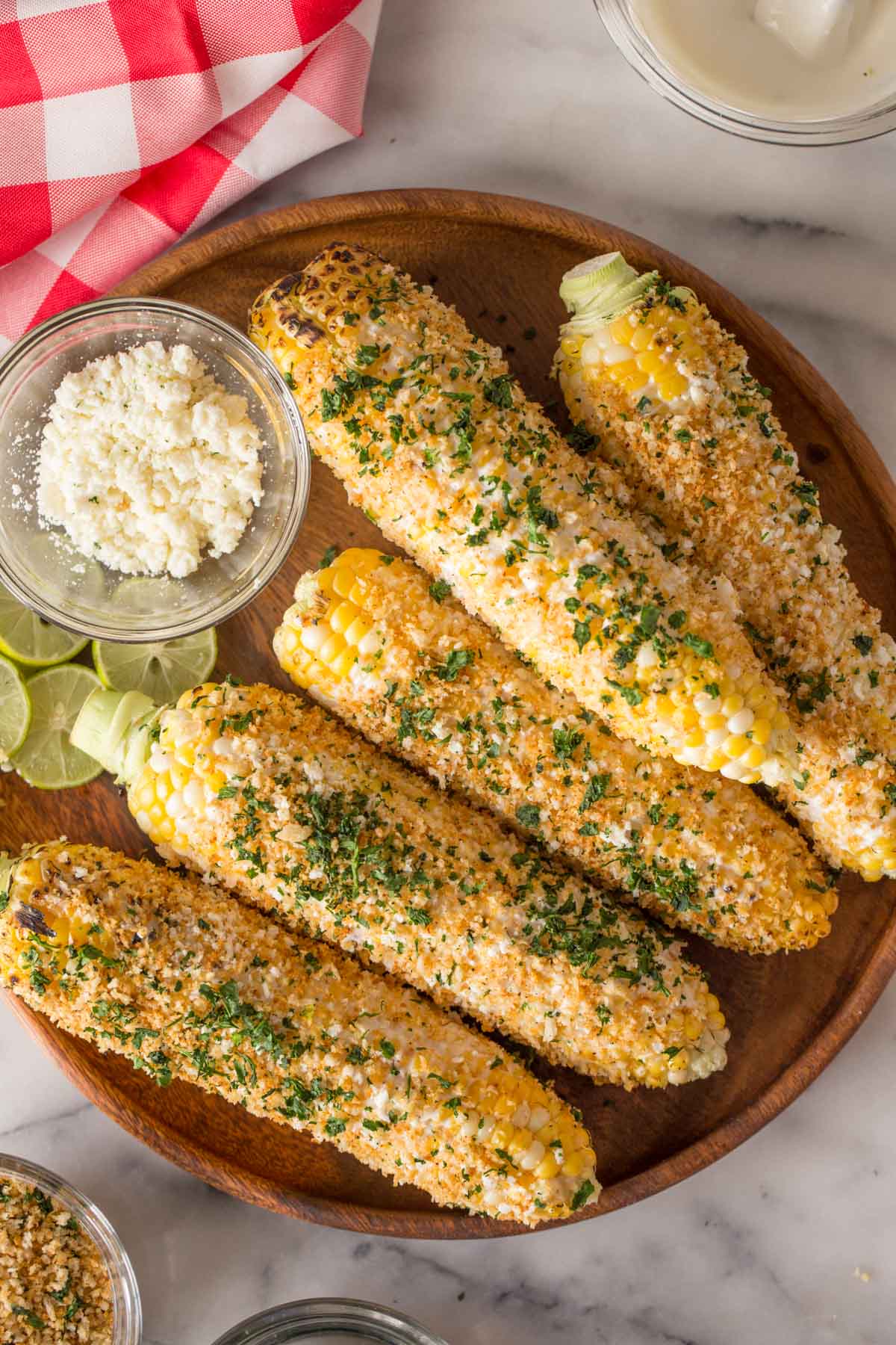 Overhead shot of Mexican Street Corn With Panko and a small glass dish of cotija cheese on a wood platter.