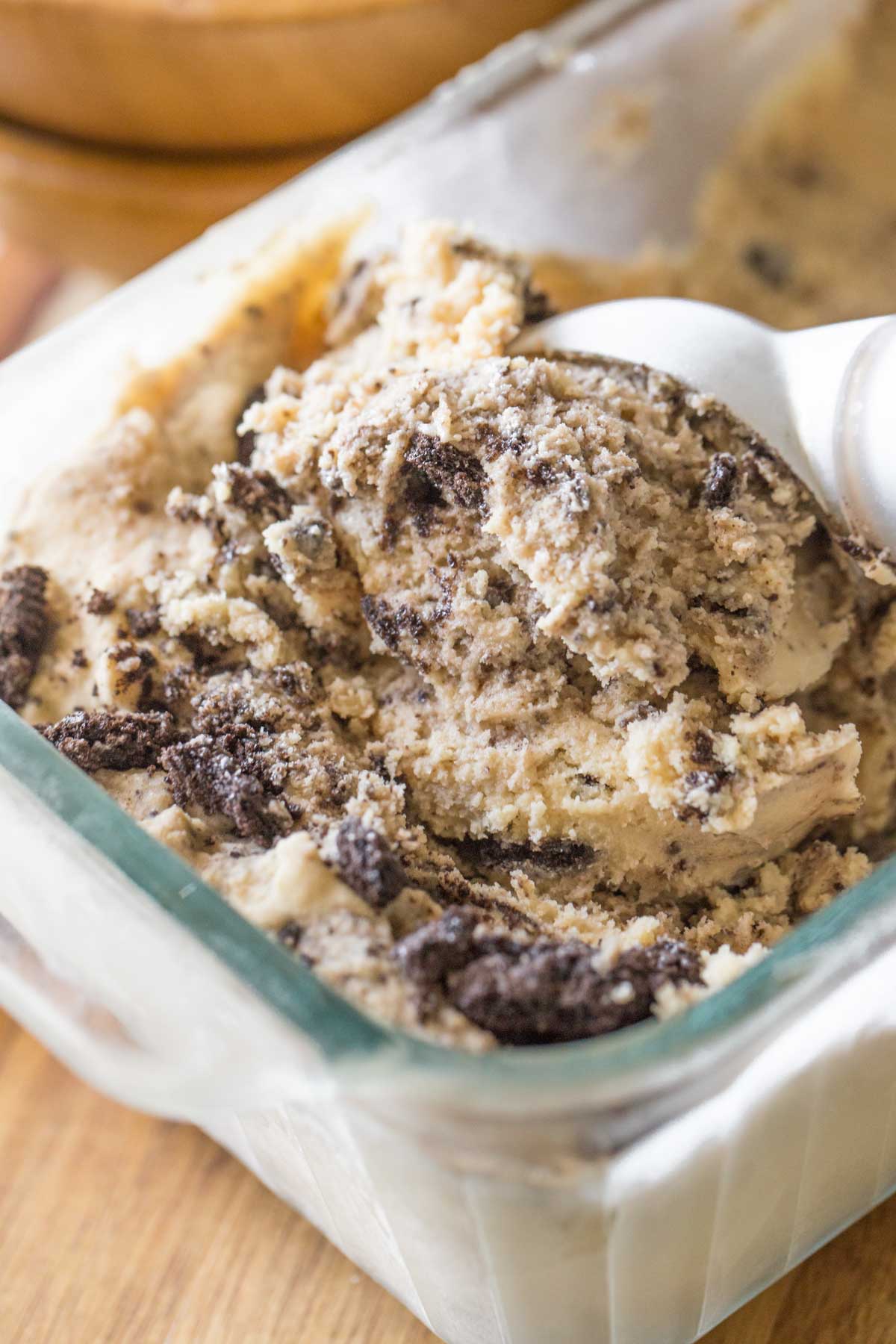 Close up shot of an ice cream scoop in a glass container of Peanut Butter Oreo Ice Cream.  