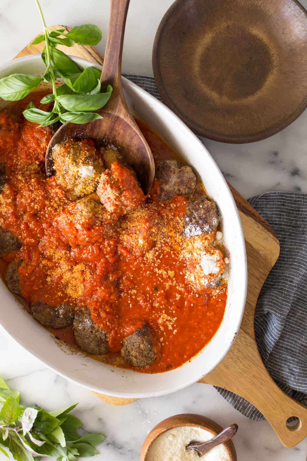 Overhead shot of Easy Broiled Italian Meatballs in a baking dish sitting on a wooden cutting board, with a wood serving spoon in the meatballs.  