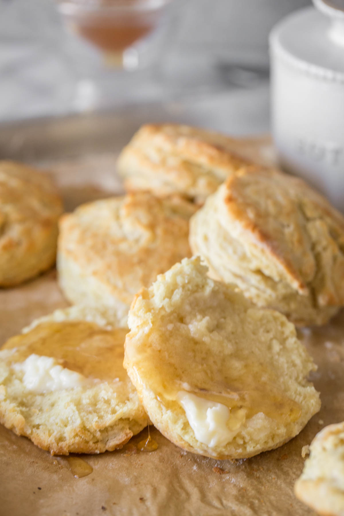Close up shot of an Easy Homemade Biscuit split open with butter and honey on top, with more biscuits in the background. 