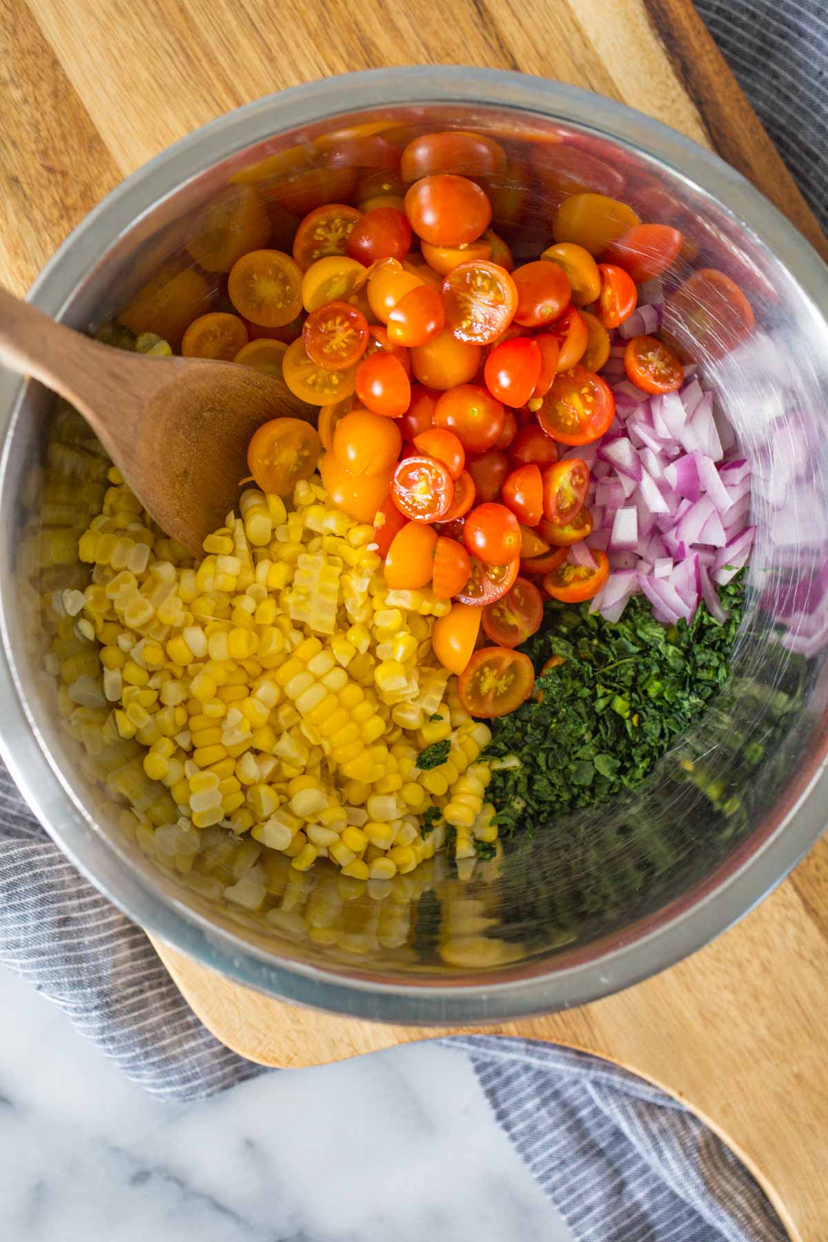 Overhead shot of a mixing bowl with some of the ingredients for Honey Lime Corn Salsa in it with a wooden spoon.  