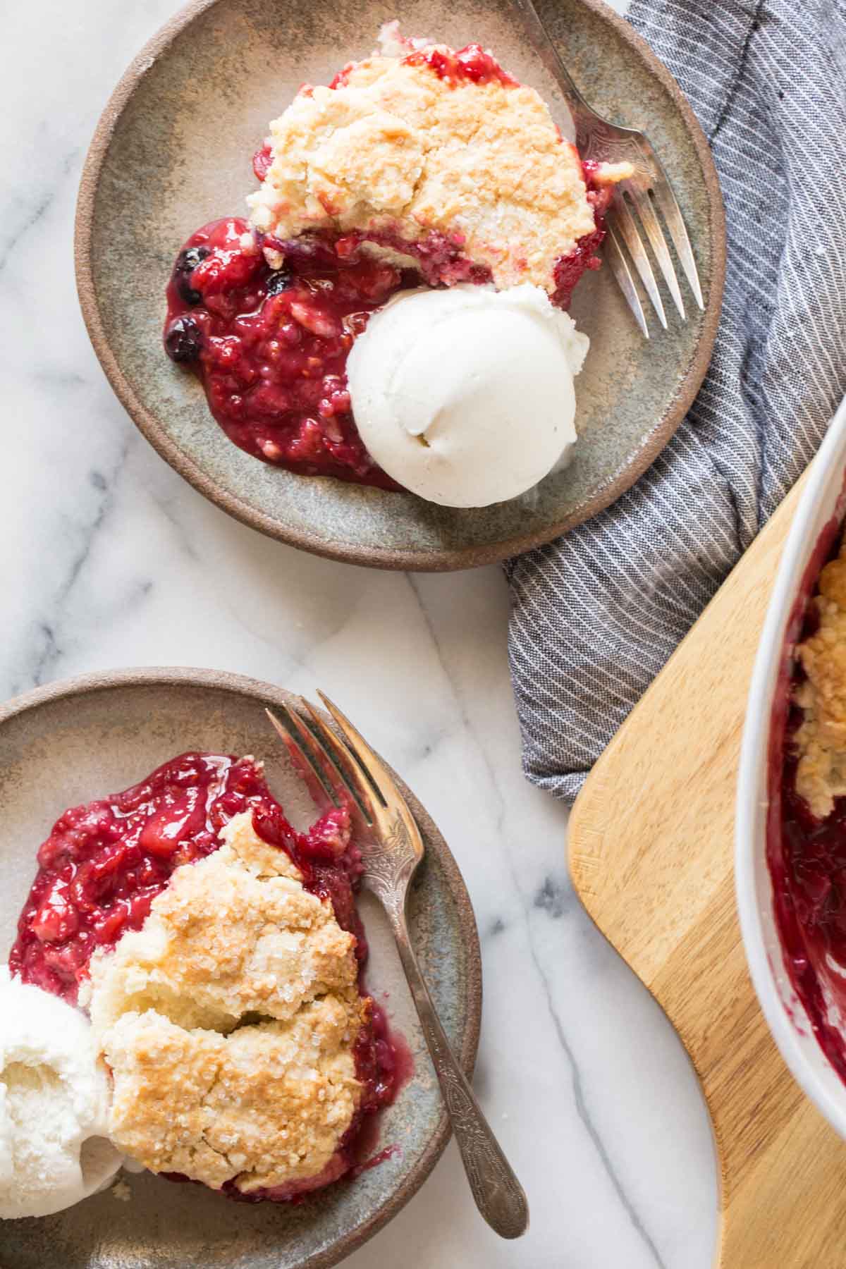 Overhead shot of two plates of Triple Berry Cobbler with a scoop of vanilla ice cream and a fork on each plate. 
