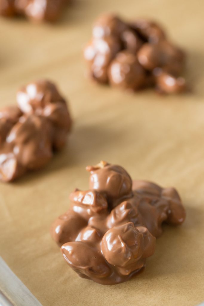 Close up shot of Chocolate Peanut Clusters on a parchment lined baking sheet.  