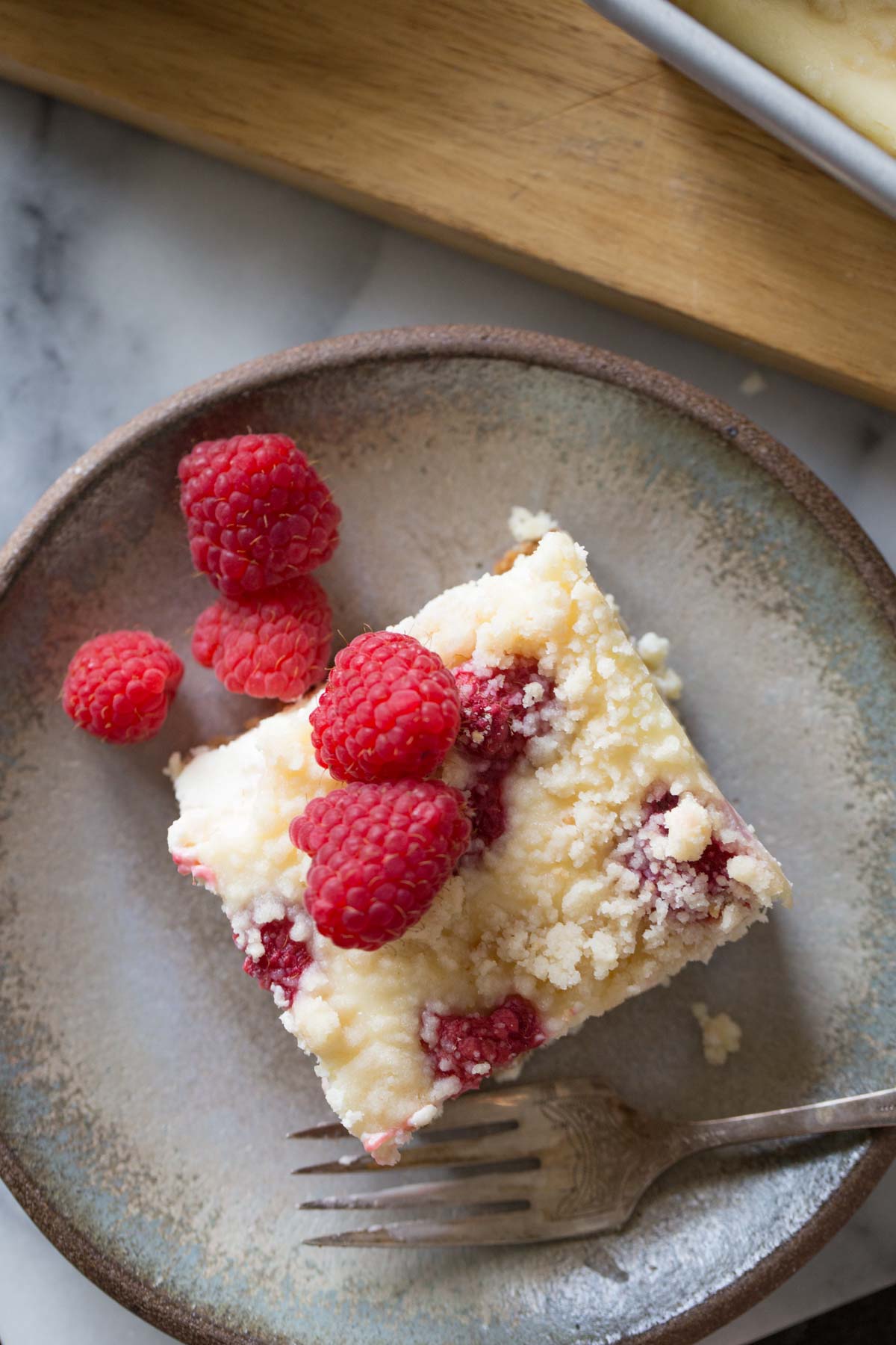 Overhead shot of a Cheesecake Bar With Berry Streusel on a plate with a fork, topped with fresh raspberries.