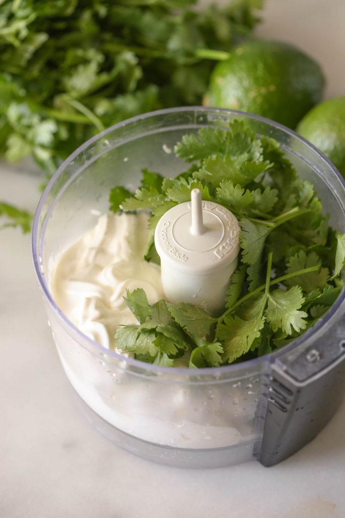 A small food processor with the ingredients for the Cilantro Lime Cream in it.  