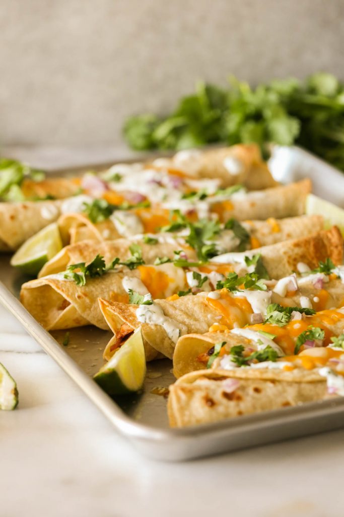 BBQ Chicken Taquitos garnished with fresh cilantro and lime wedges on a baking sheet. 