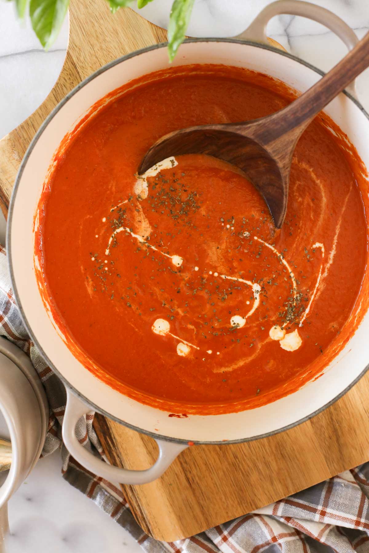 Overhead shot of a pot of Creamy Balsamic Tomato Soup with a wood serving spoon in it, sitting on wood cutting board.  