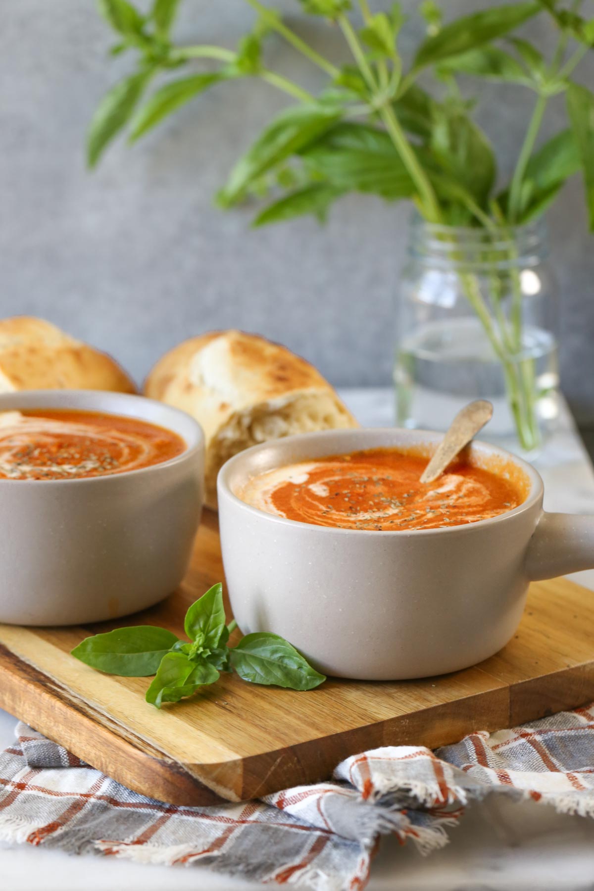 Two bowls of Creamy Balsamic Tomato Soup on a wood cutting board with two torn pieces of crusty bread.  