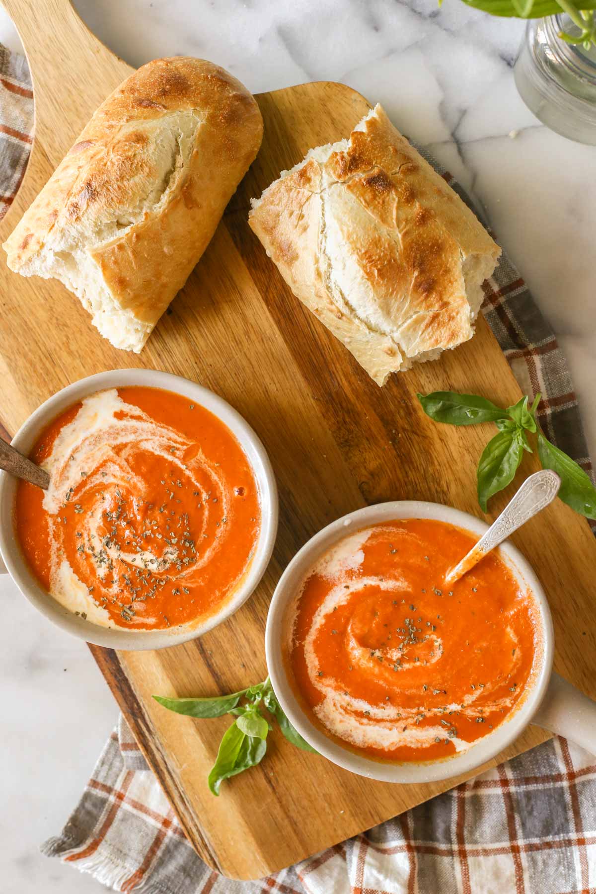Overhead shot of two bowls of Creamy Balsamic Tomato Soup on a wood cutting board, along with two pieces of torn crusty bread.  