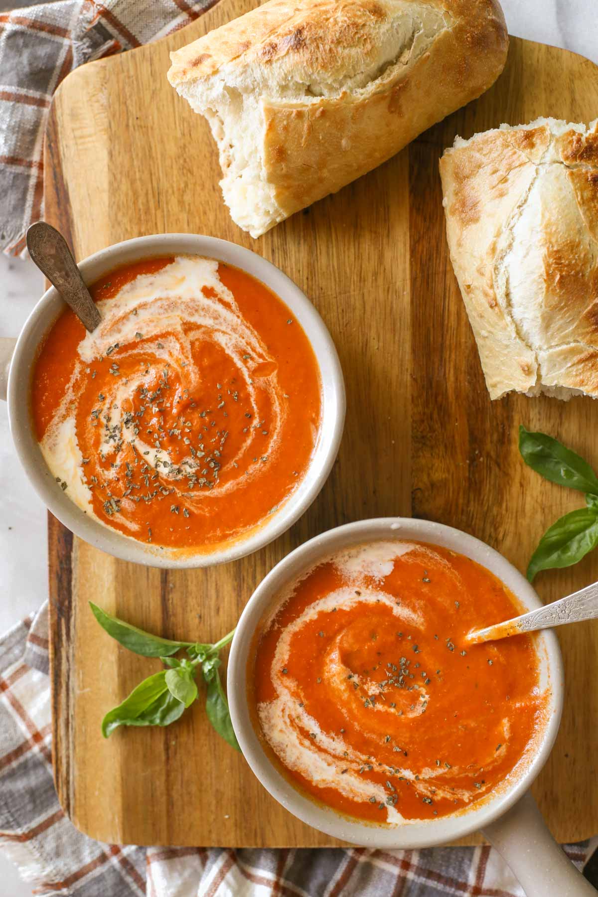 Overhead shot of two bowls of Creamy Balsamic Tomato Soup on a wood cutting board, along with two pieces of torn crusty bread.  