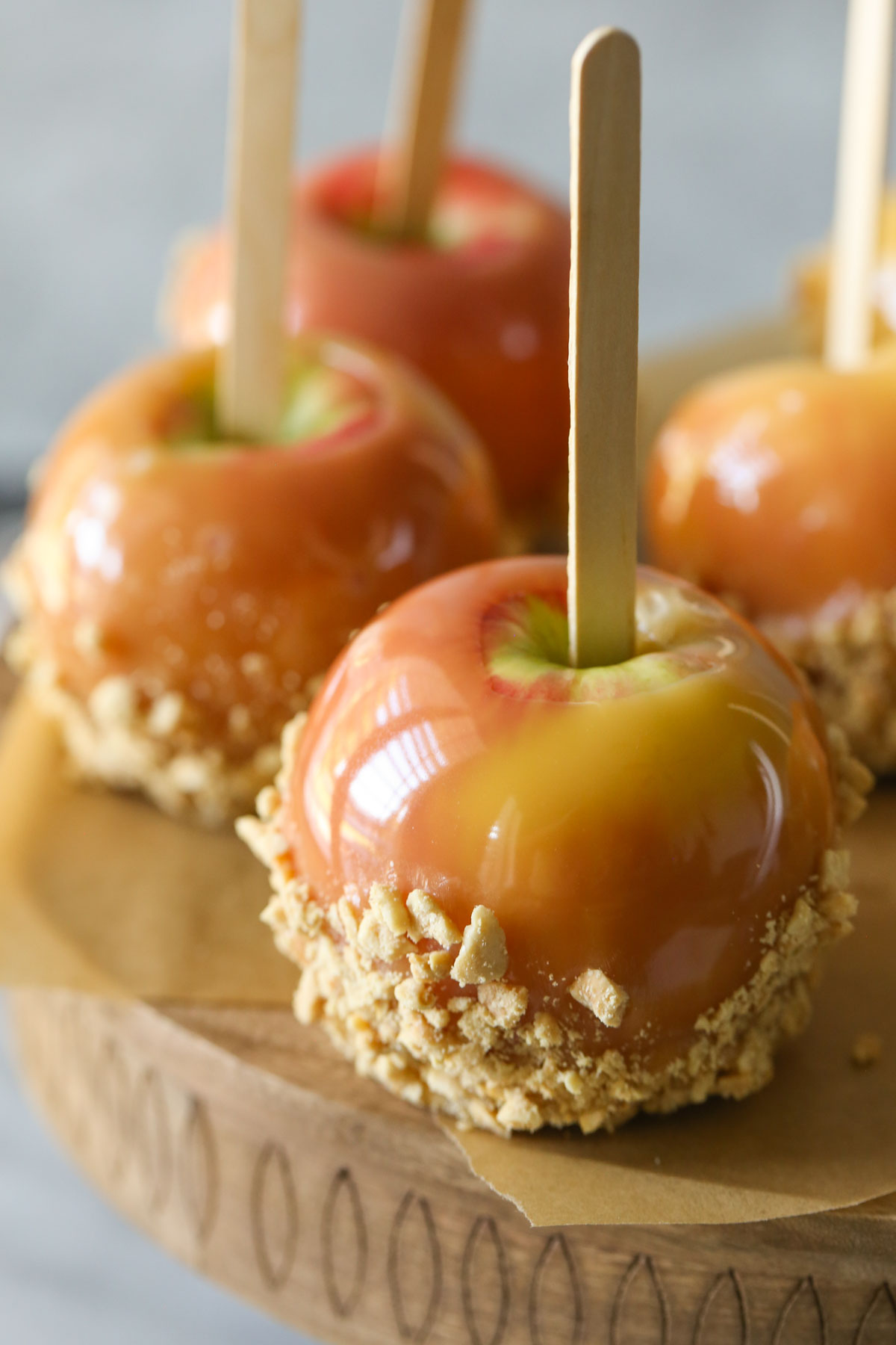 Close up shot of Homemade Caramel Apples on parchment paper on top of a wood stand.  